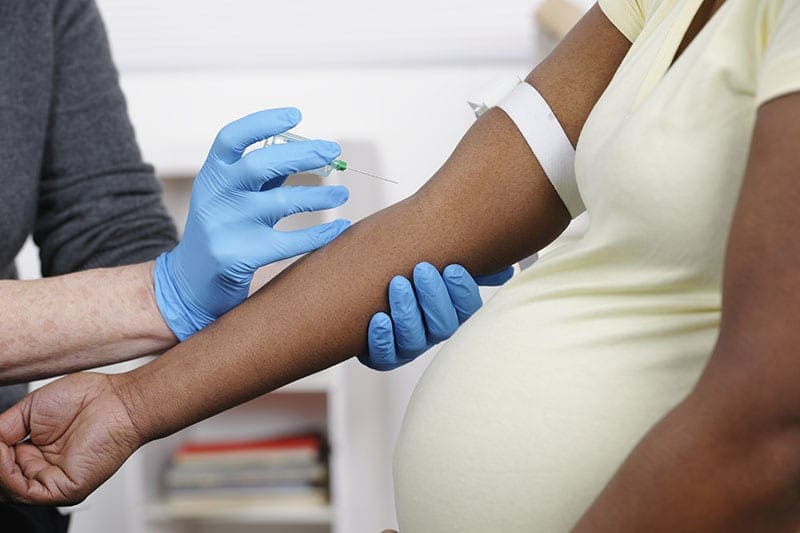 an image of a pregnant woman having blood drawn by a nurse wearing blue rubber gloves