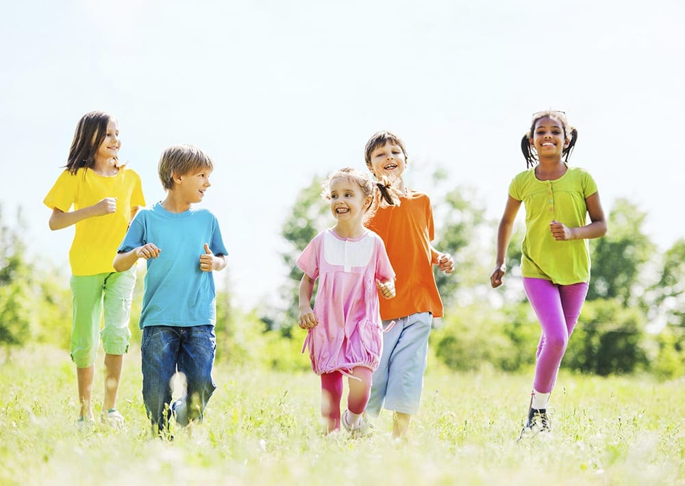 a long distance image of a group of children running through a grassy field